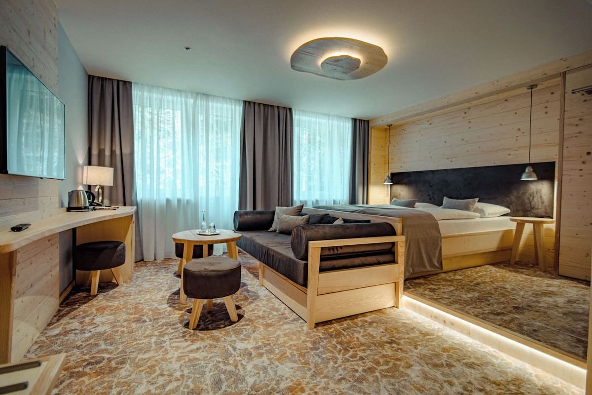 A modern hotel room with a bed, a desk, a sofa, and a small table.