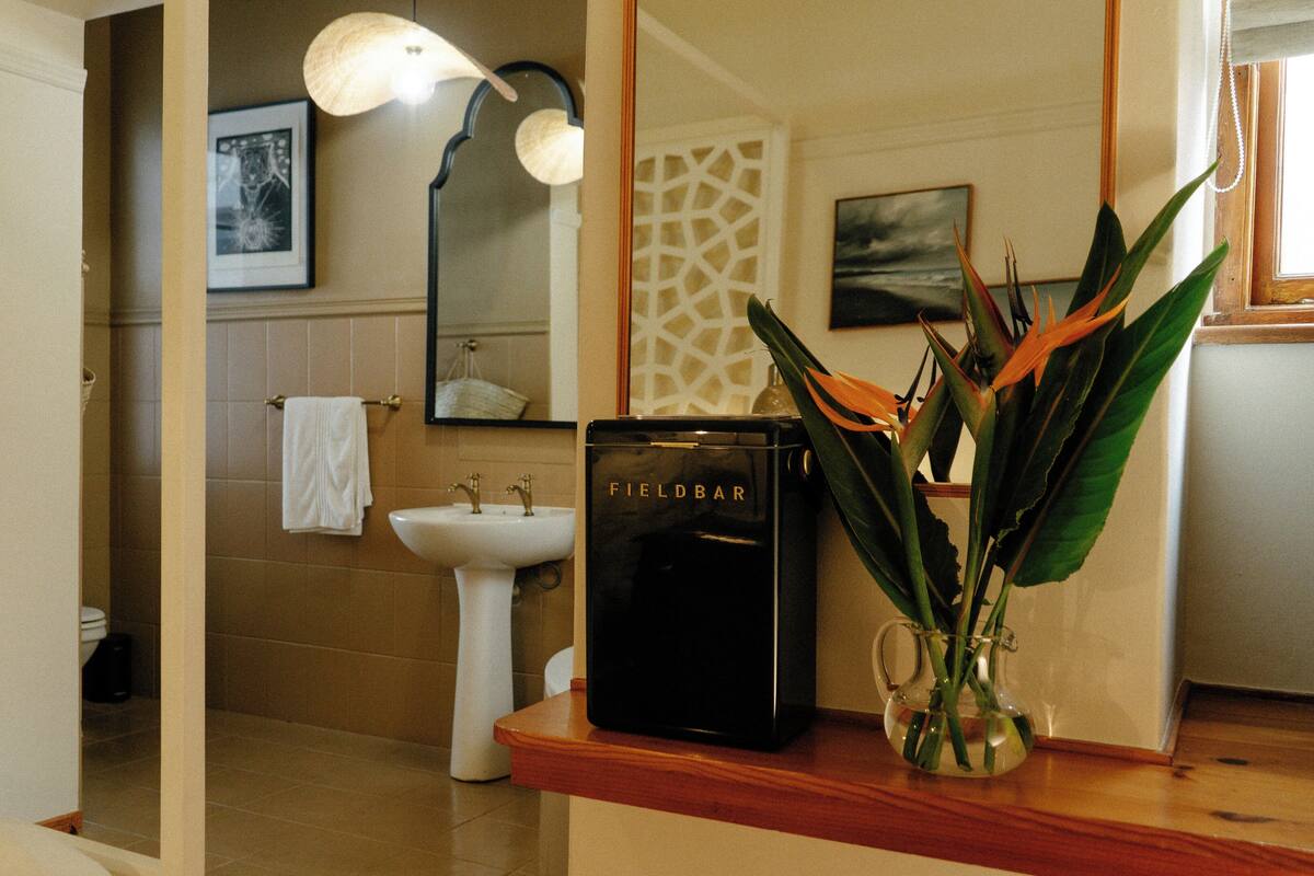 A bathroom with a sink, mirror, towel rack, and a Fieldbar coffee machine.