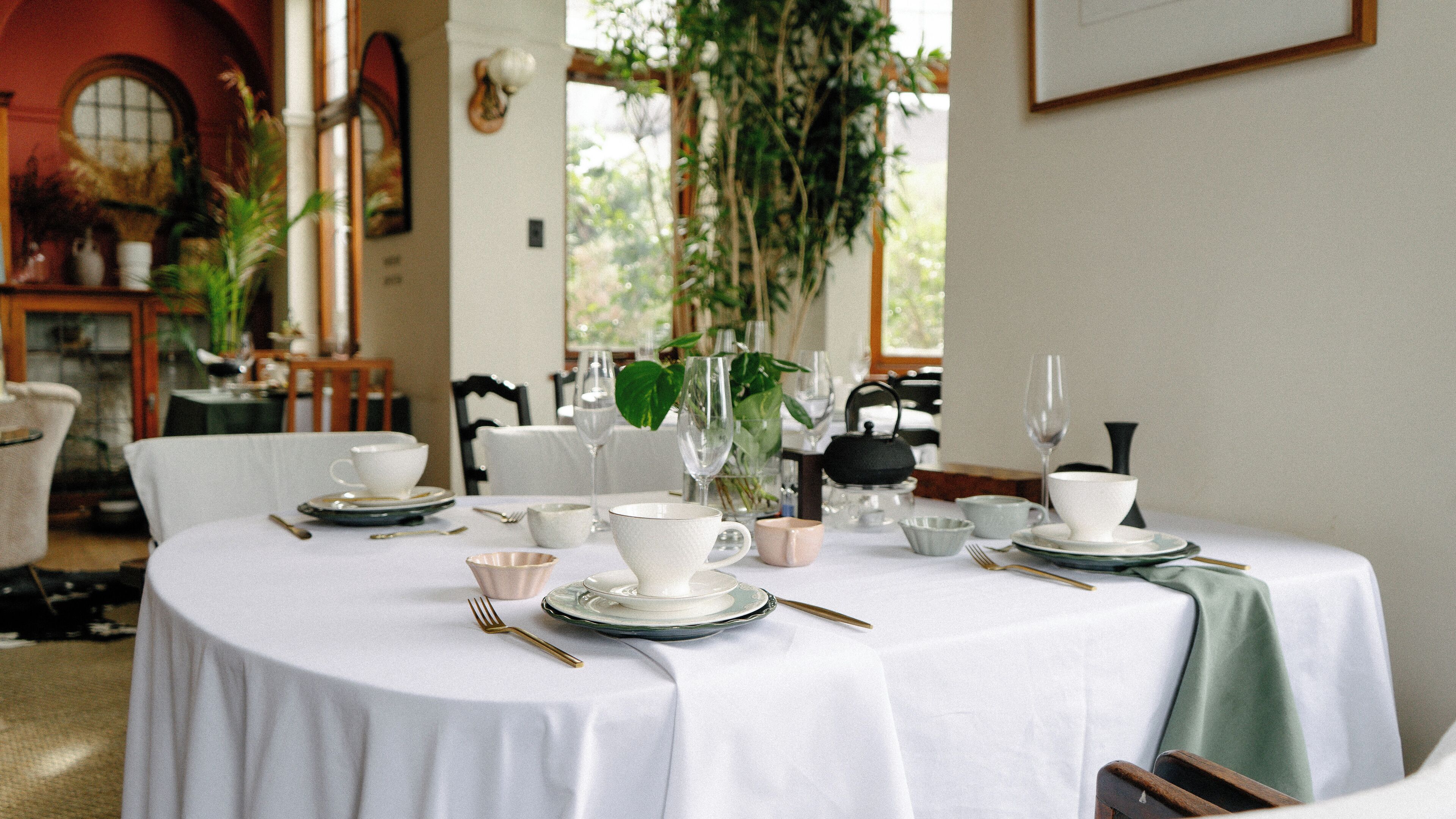 Taula de menjador coberta amb estovail blanc, plats, tasses i coberts.