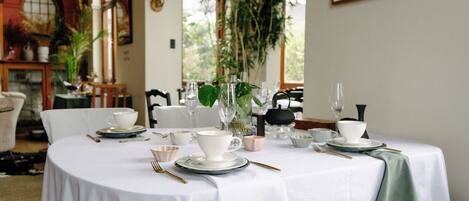 A dining table set with white tablecloth, plates, cups, and cutlery.