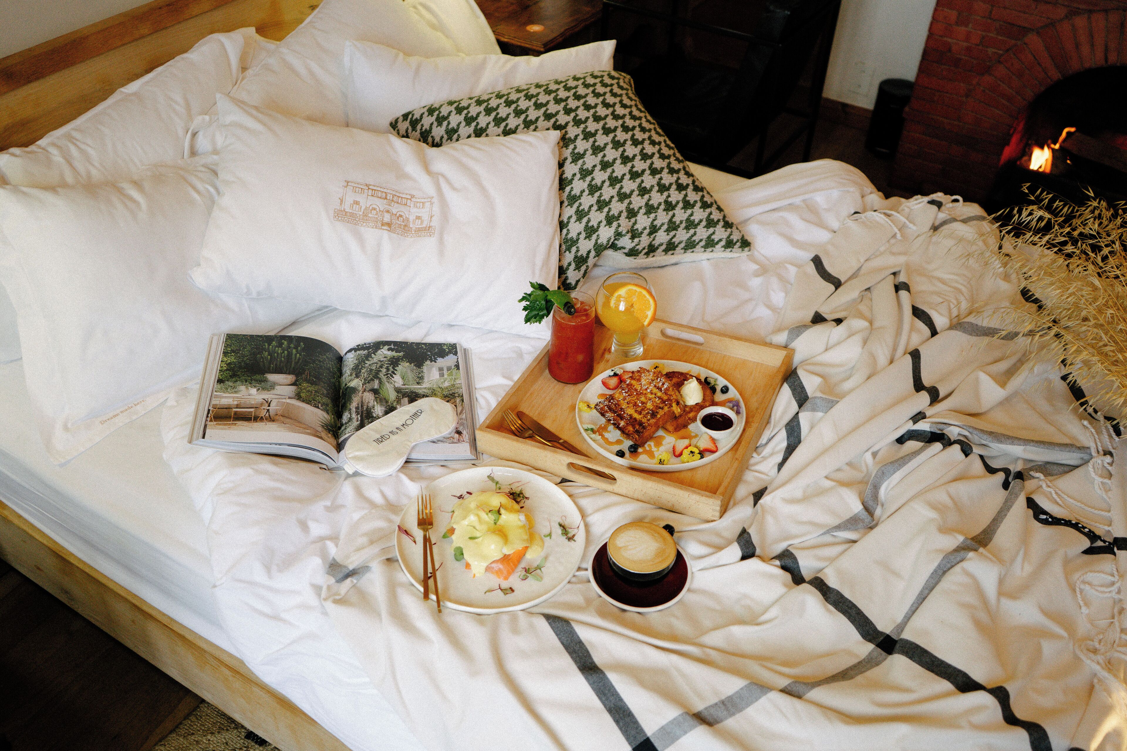 A neatly made bed with a book, a tray with breakfast items, and a cup of coffee.