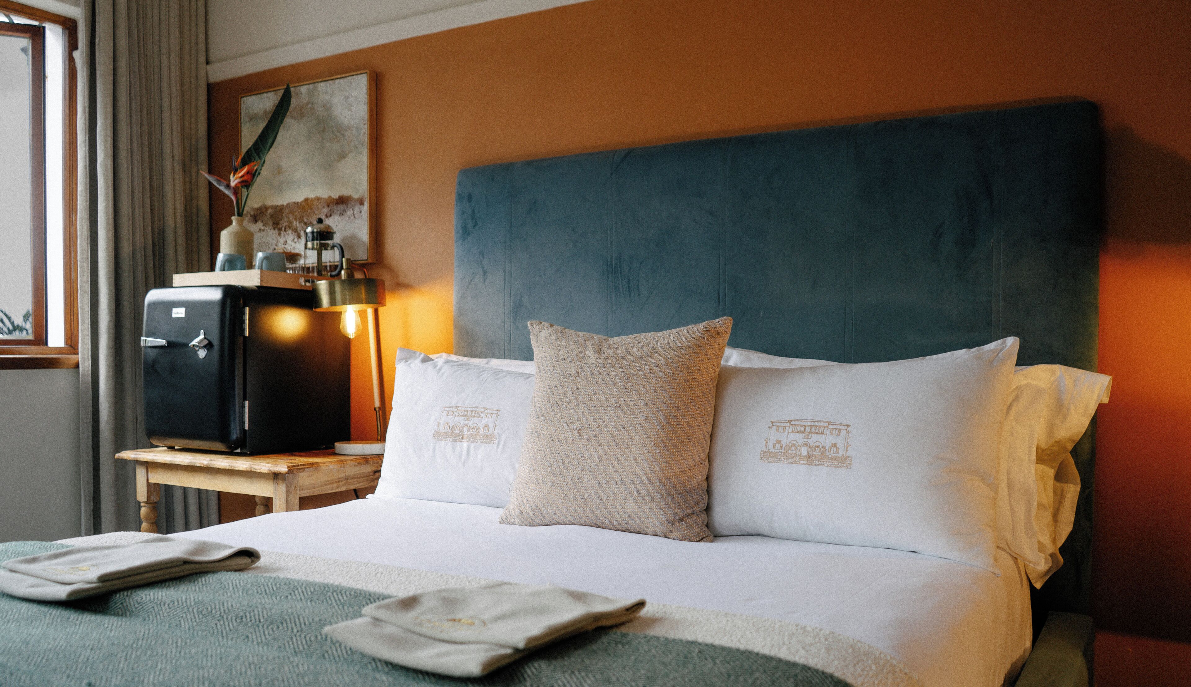A neatly made bed with two pillows, a bedside table with a lamp, and a vintage radio.