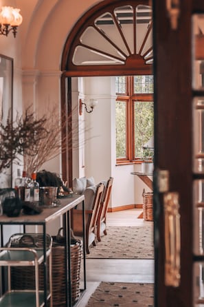 Ein gemütliches Zimmer mit einer Holztreppe, einem Essbereich mit Stühlen und einem Tisch sowie einem großen Fenster mit Blick auf Bäume.