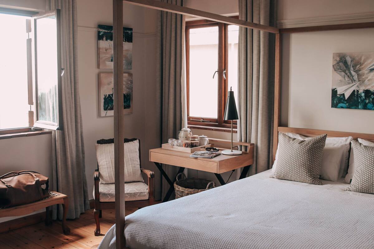 A neatly arranged bedroom with a bed, a bedside table, a chair, a desk, and a window with curtains.