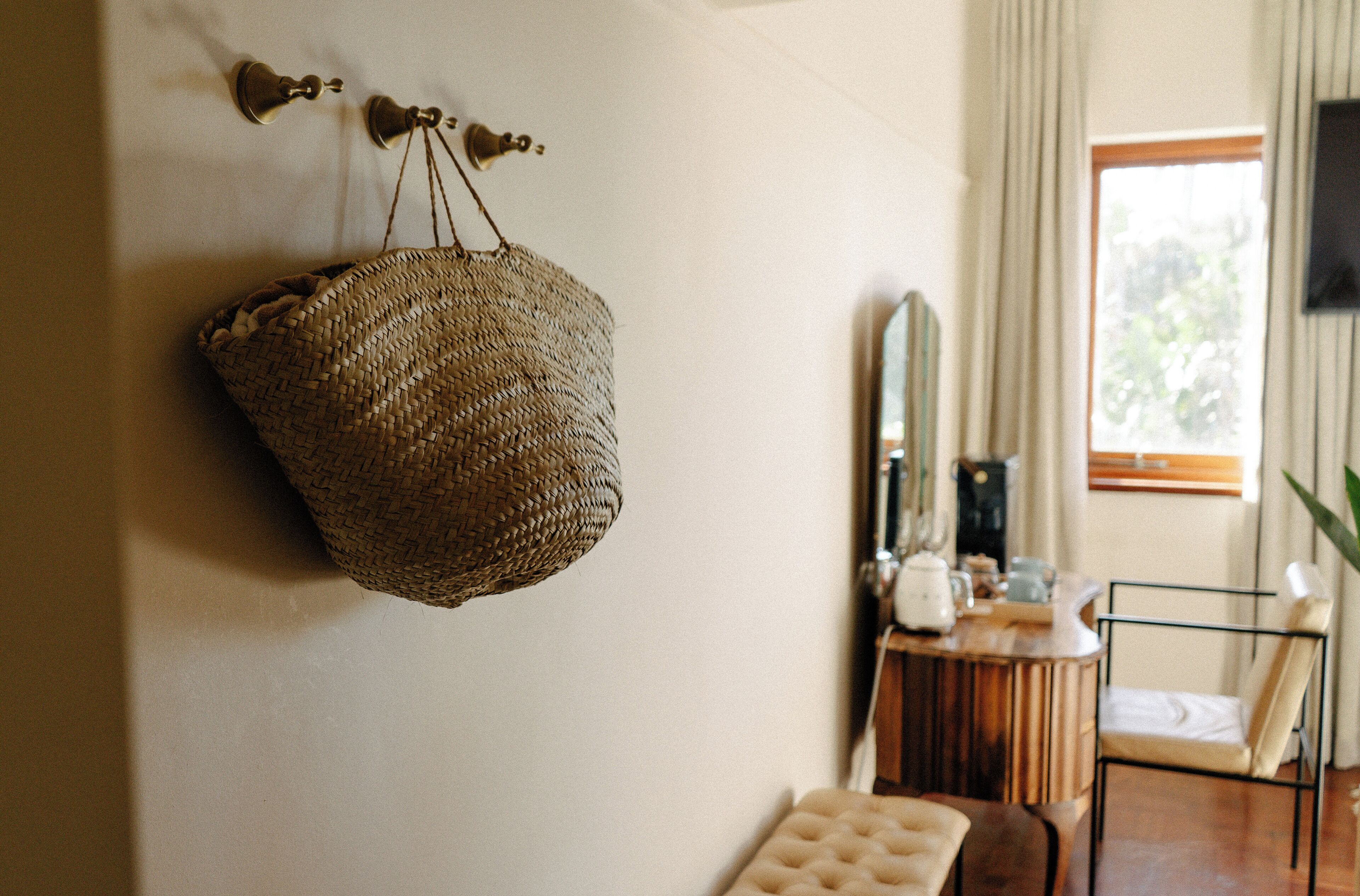 A room with a woven basket hanging on the wall, a wooden side table with a mirror, and a chair.