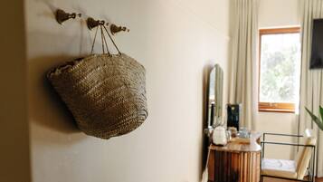 A room with a woven basket hanging on the wall, a wooden side table with a mirror, and a chair.