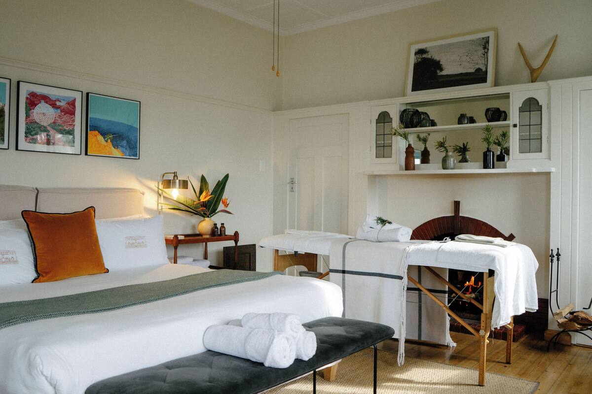 A hotel room with a large bed, a bench, a fireplace, and a shelf with decorative items.