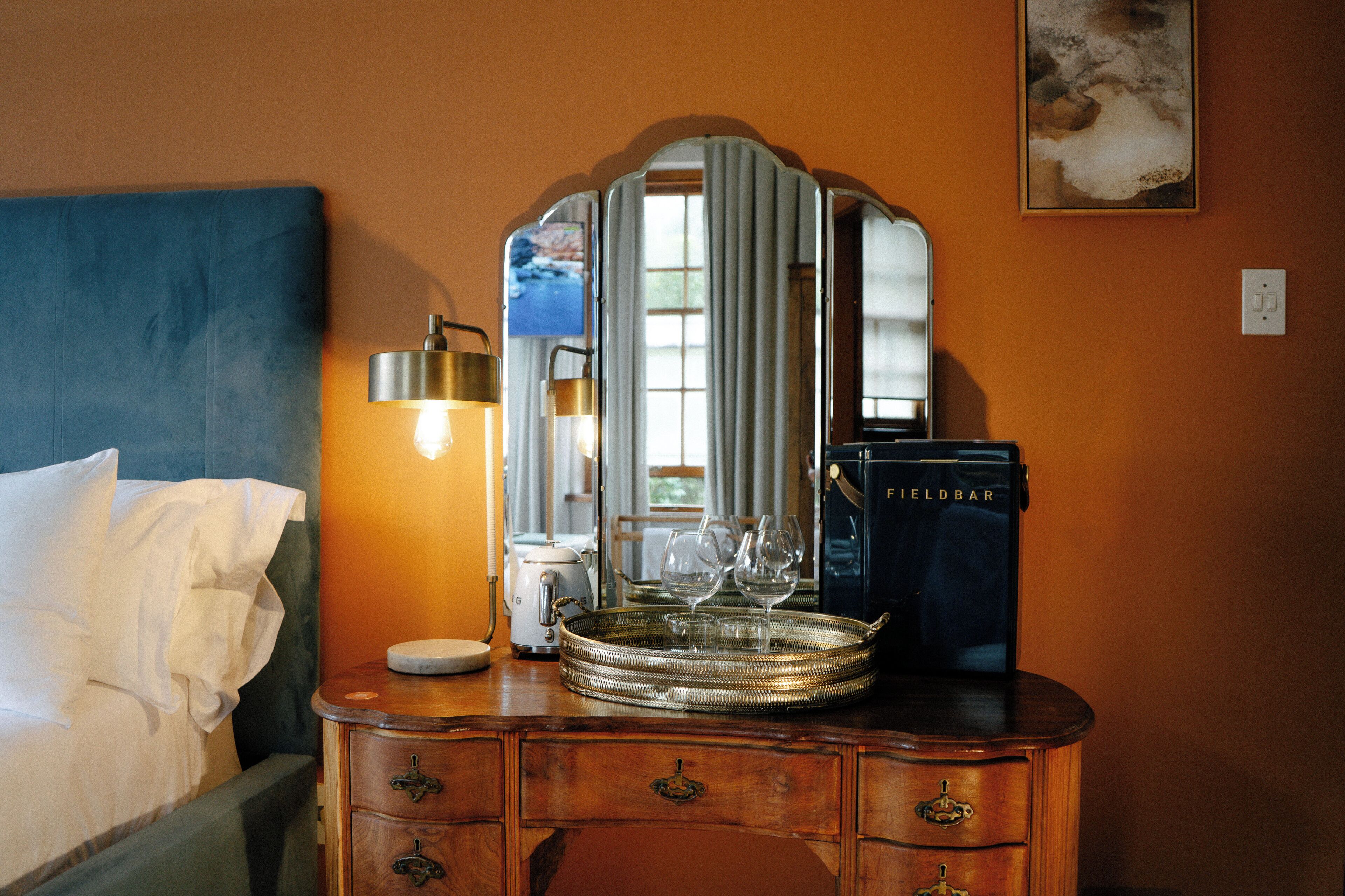 A hotel room with a bed, dresser, mirror, lamp, and a tray with wine glasses.