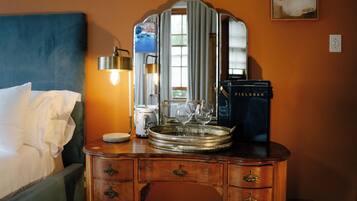 A hotel room with a bed, dresser, mirror, lamp, and a tray with wine glasses.