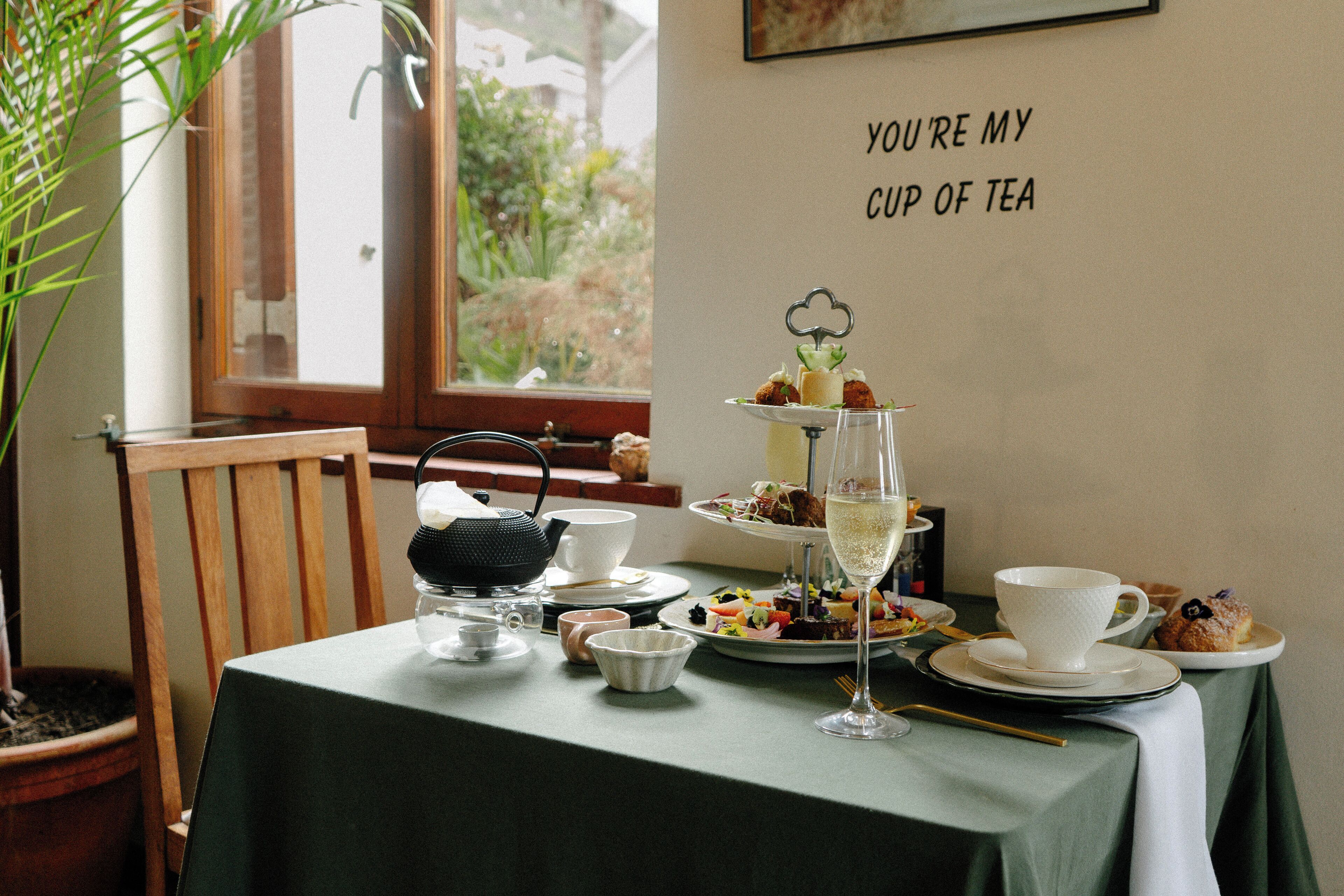 A table set for tea with a tiered dessert display, a teapot, cups, and a wall sign.