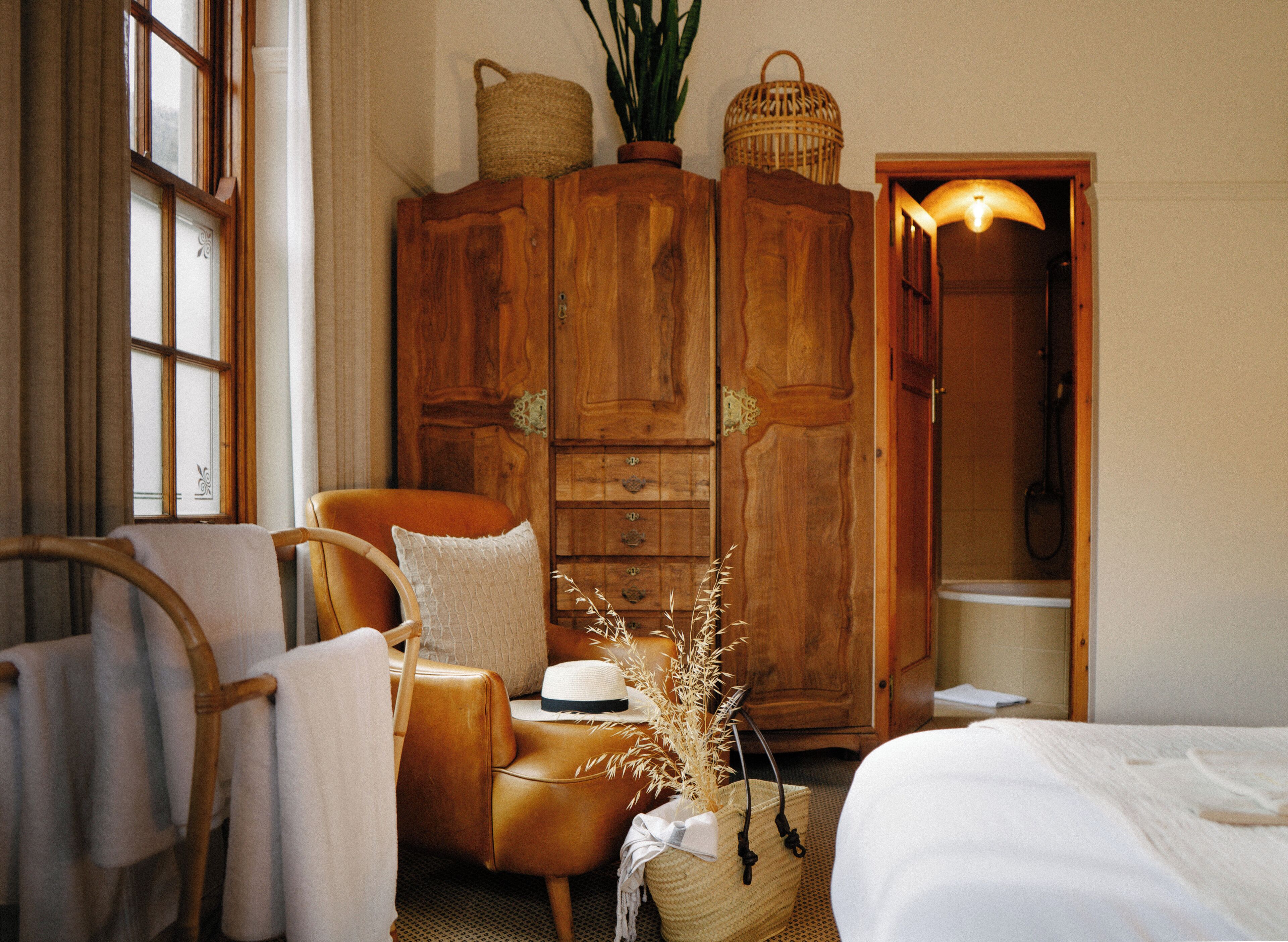 A cozy room with a wooden wardrobe, a leather armchair, a bed, and a window with curtains.