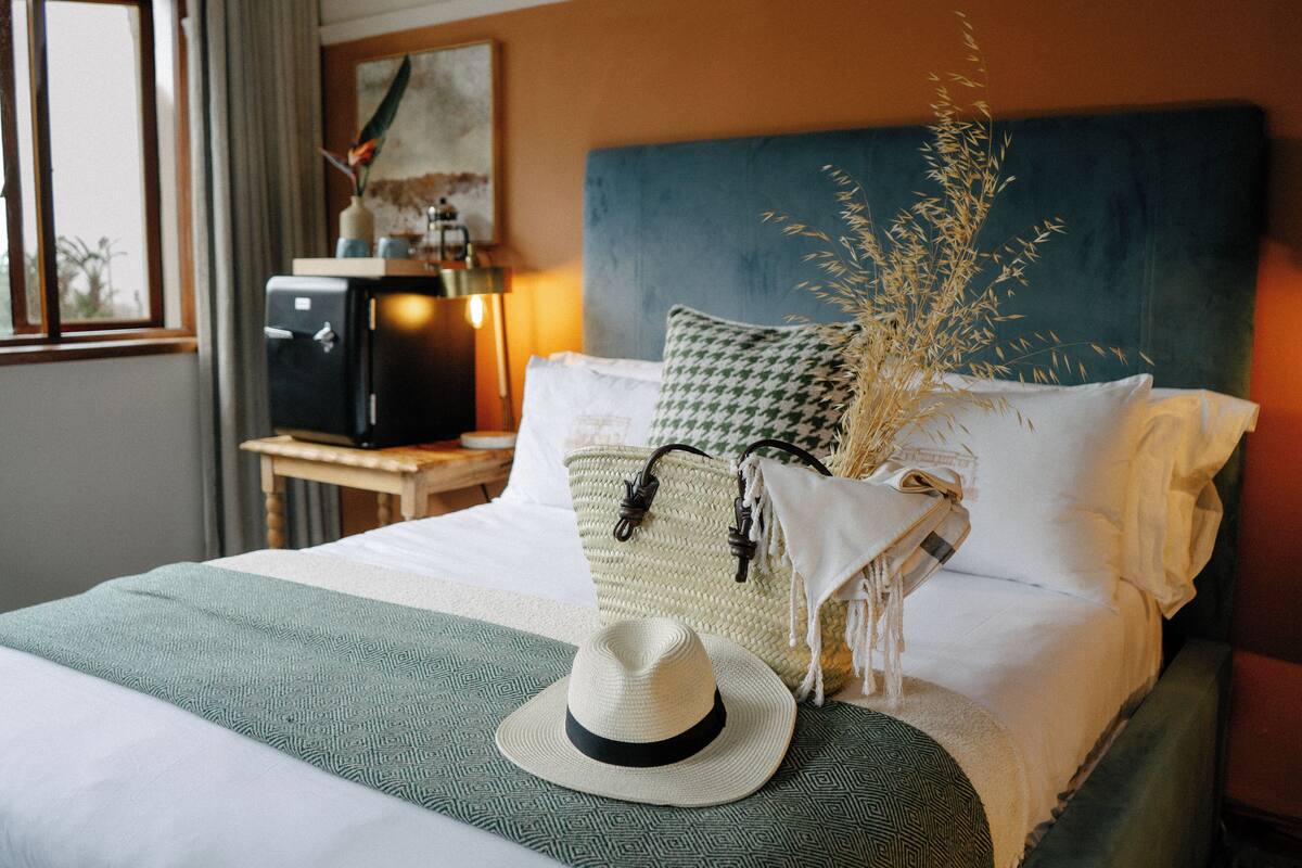 A neatly made bed with a hat, pillows, and a decorative plant.