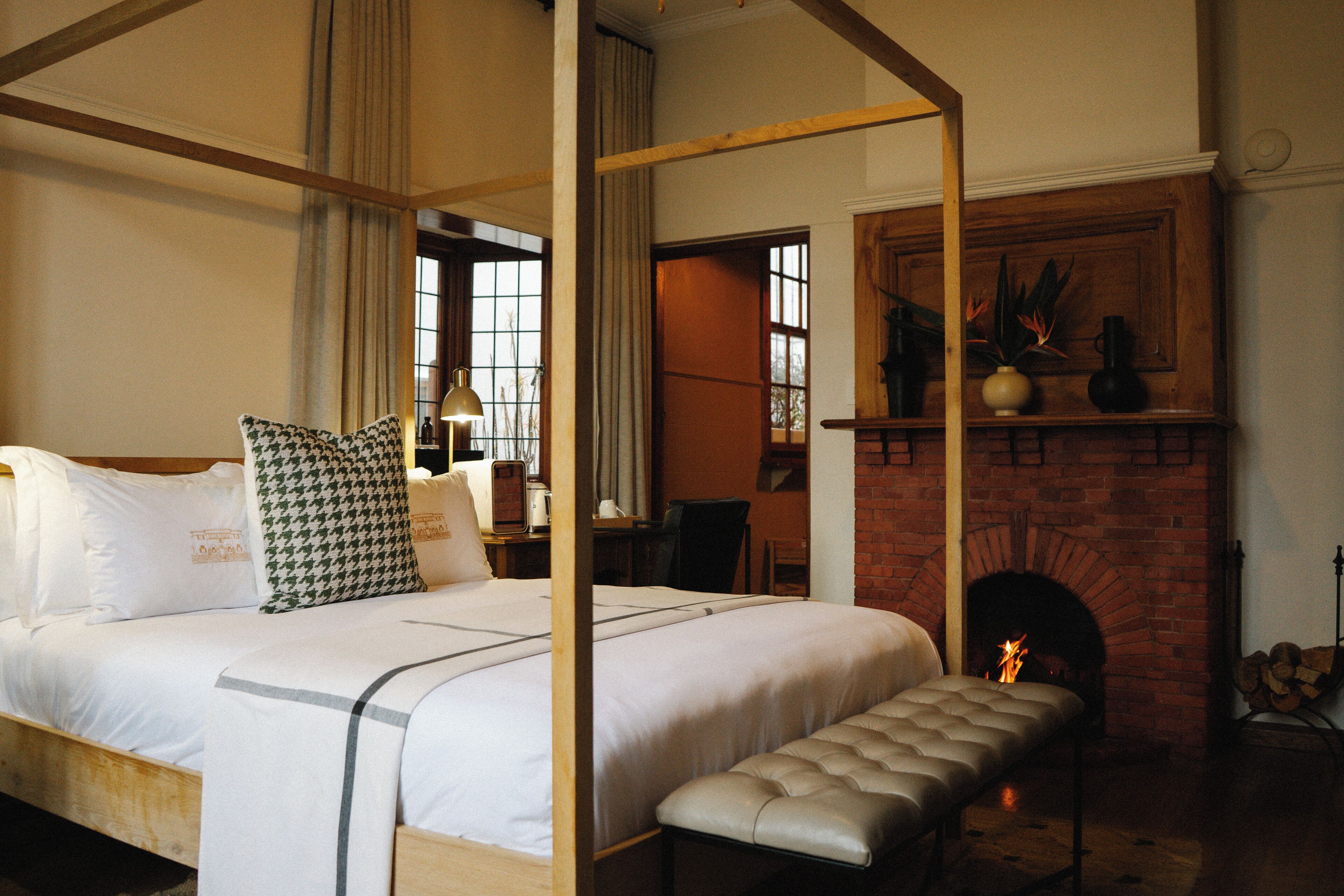 Una habitación con cama con dosel, un banco, una chimenea y un escritorio con una silla.
