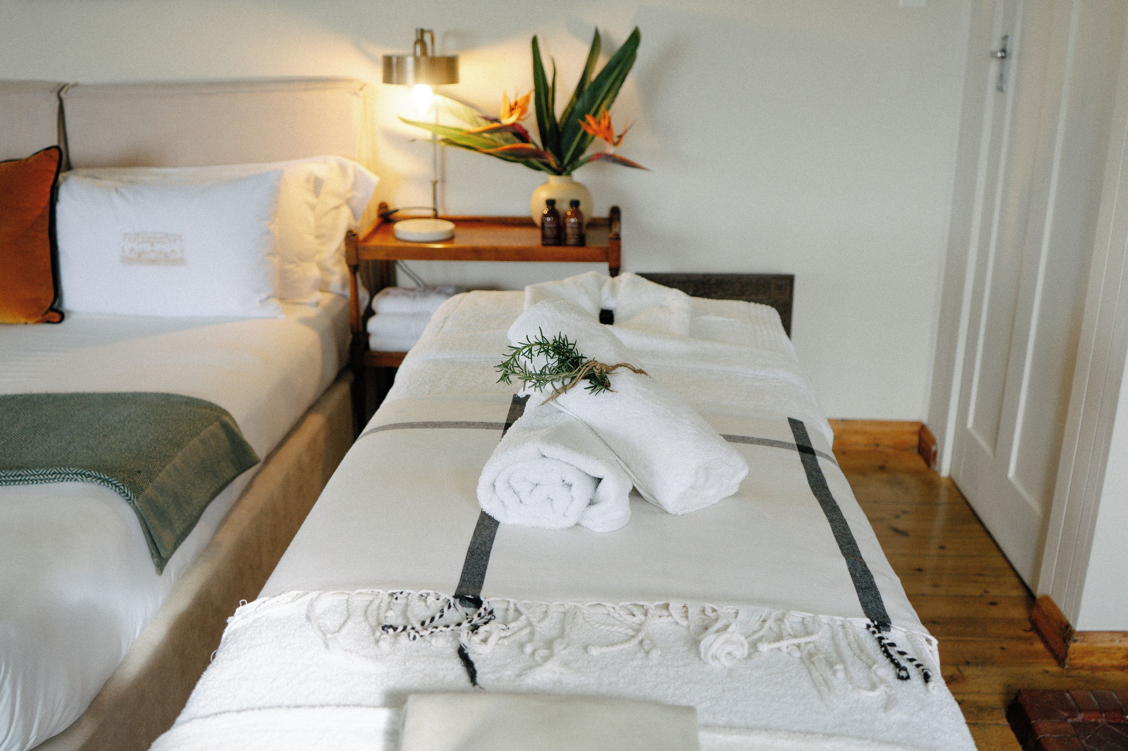 A hotel room with a bed, a bedside table with a lamp, a vase with flowers, and a wooden floor.