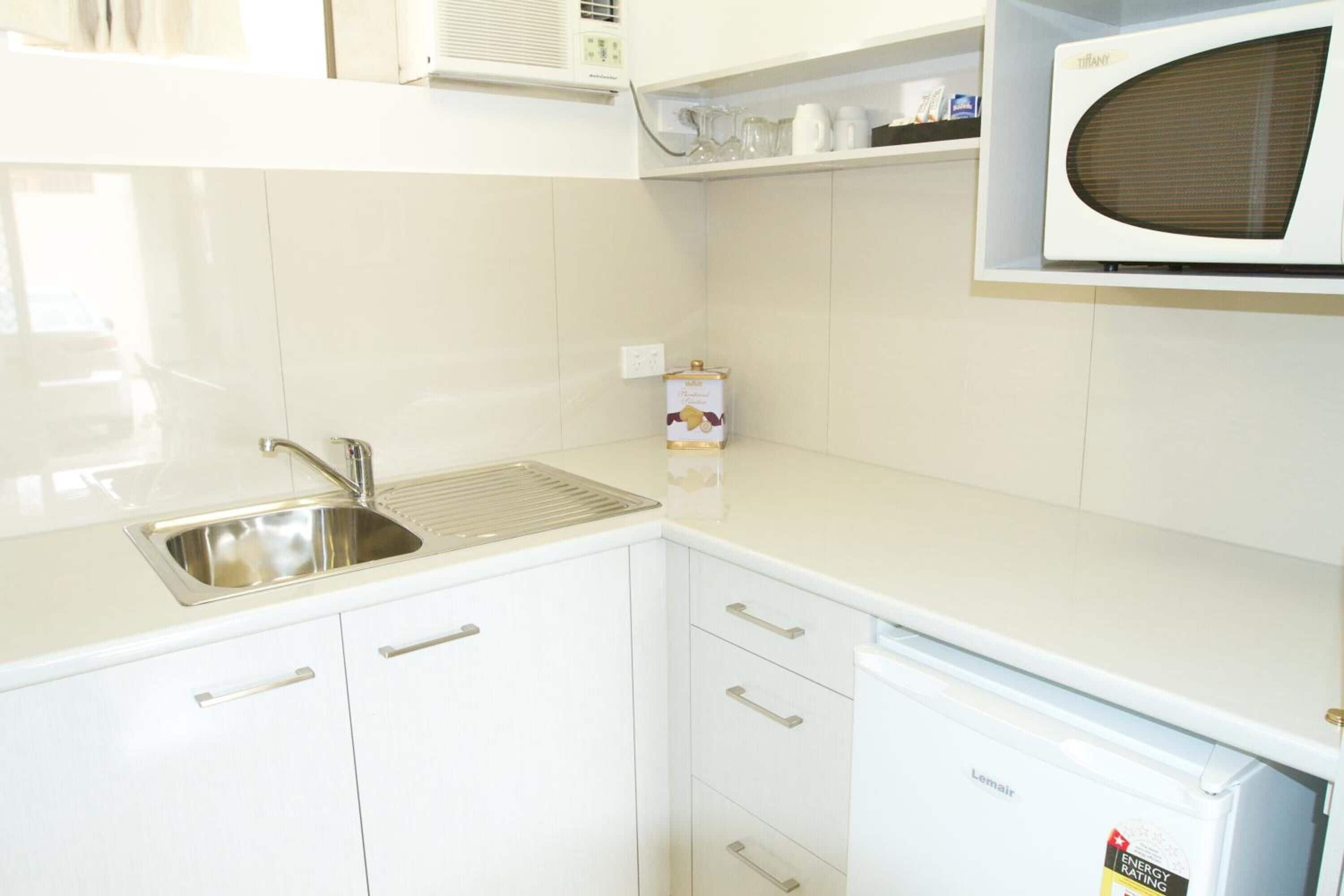 Una cocina con gabinetes blancos, un lavamanos de acero inoxidable, un microondas y un lavavajillas.