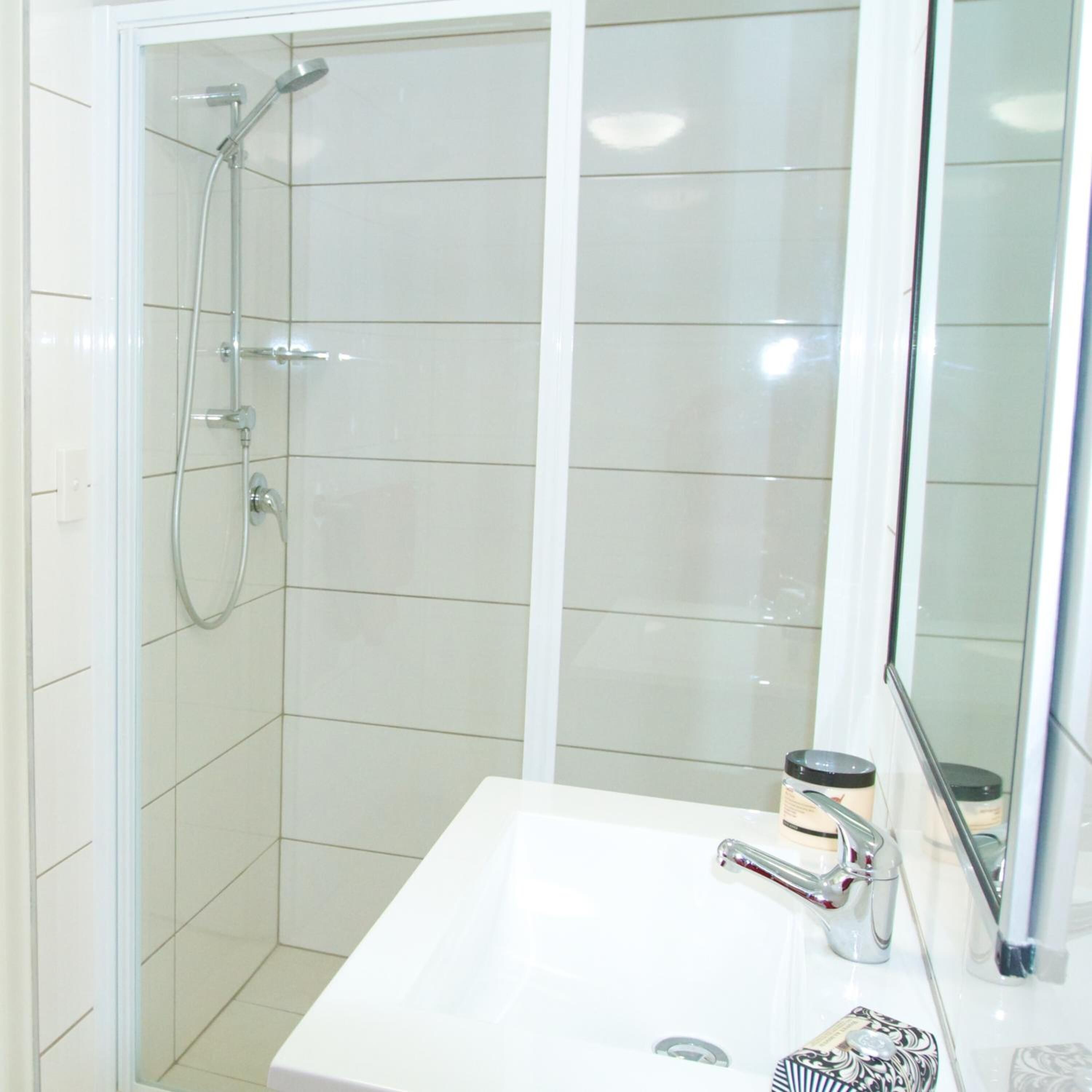 A bathroom with a shower enclosure, a sink, and a mirror.