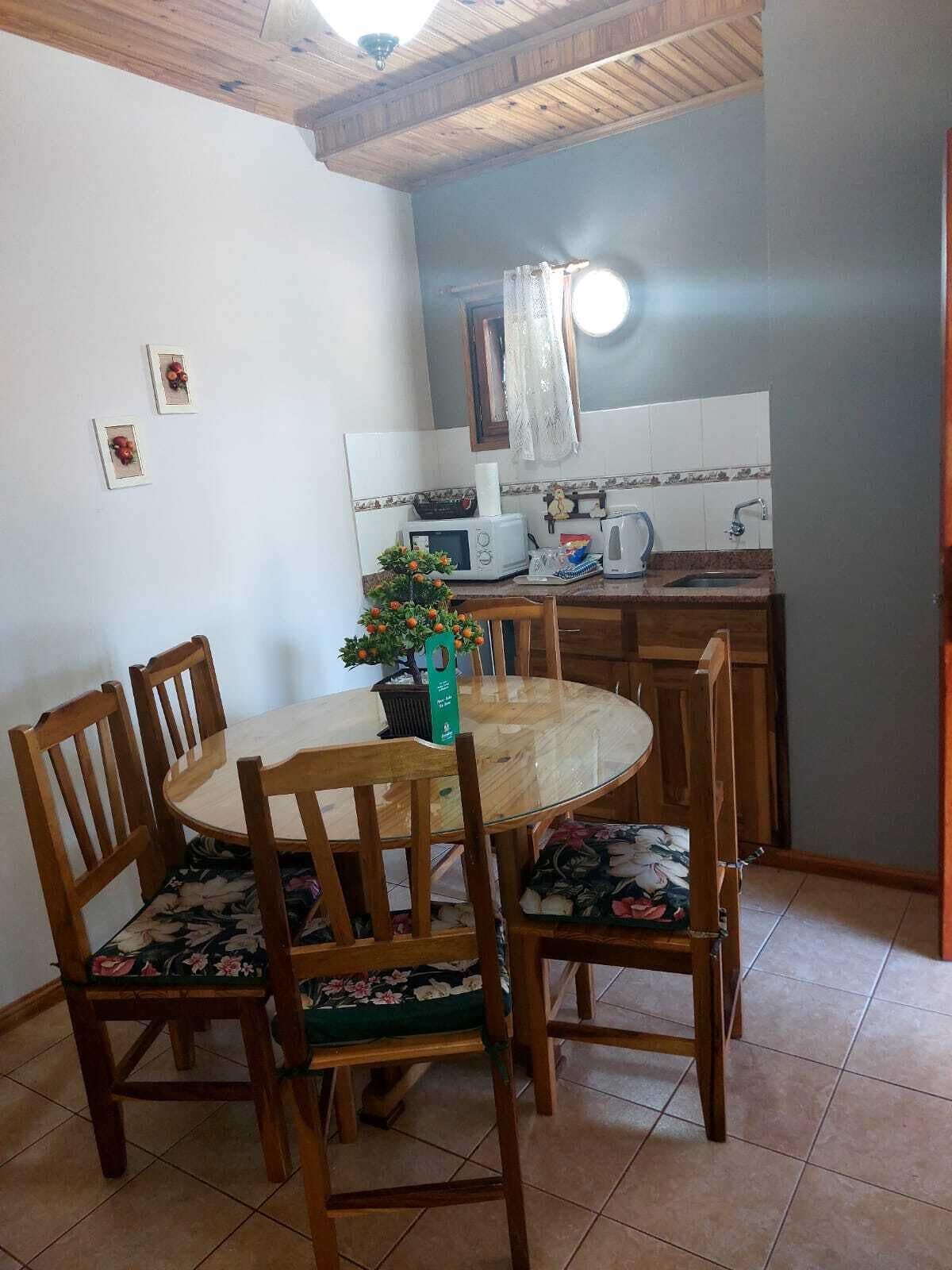 Een eetgedeelte met een ronde tafel en vier stoelen, een kleine potplant en een keuken met een magnetron, broodrooster en spoelbak.