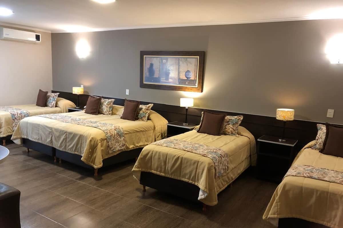 Ein Hotelzimmer mit vier nebeneinanderliegenden Betten, jeweils mit Kopfteil und Nachttischen.