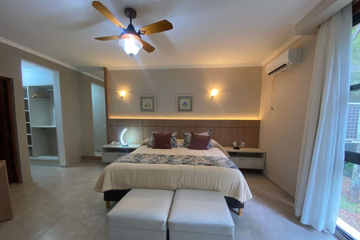 Ein Schlafzimmer mit einem Bett, Nachttischen, einem Deckenventilator und einem Fenster mit Vorhängen.