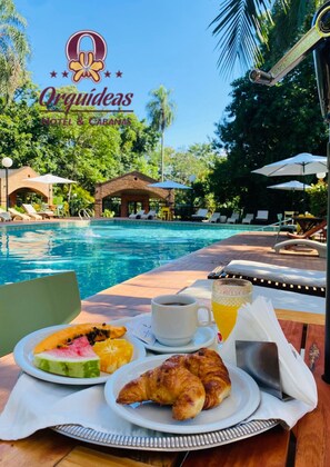 Frühstück am Pool mit einem Croissant, Obst, Kaffee und Saft.