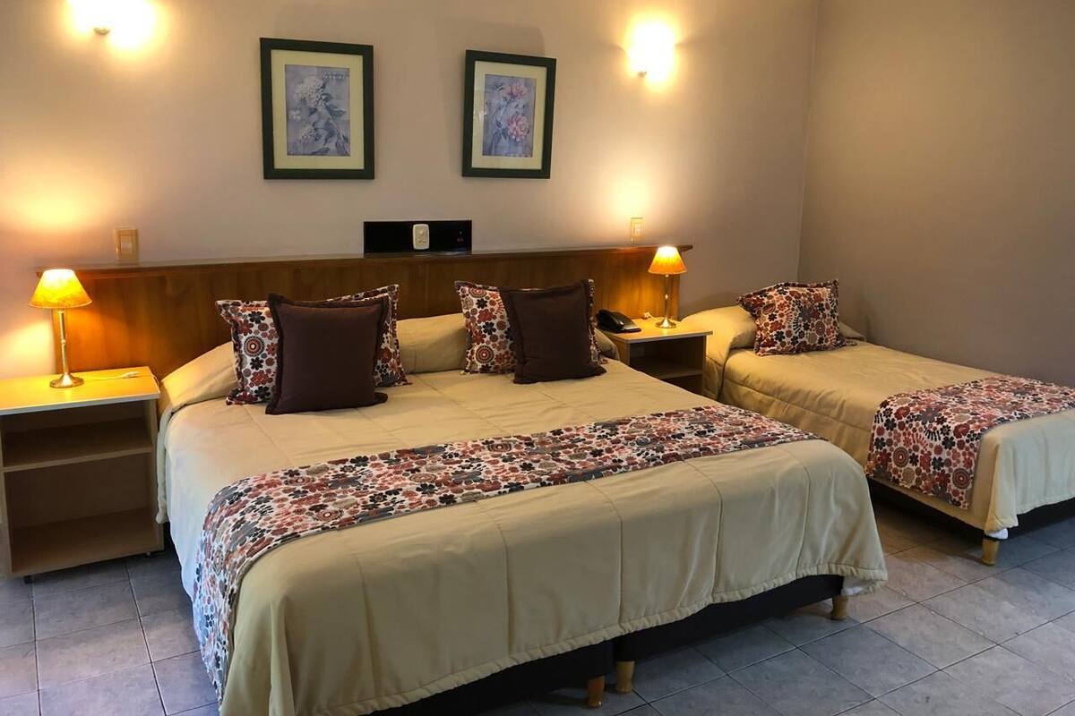 Ein Hotelzimmer mit zwei Betten, einem Nachttisch mit Lampe und zwei gerahmten Bildern an der Wand.