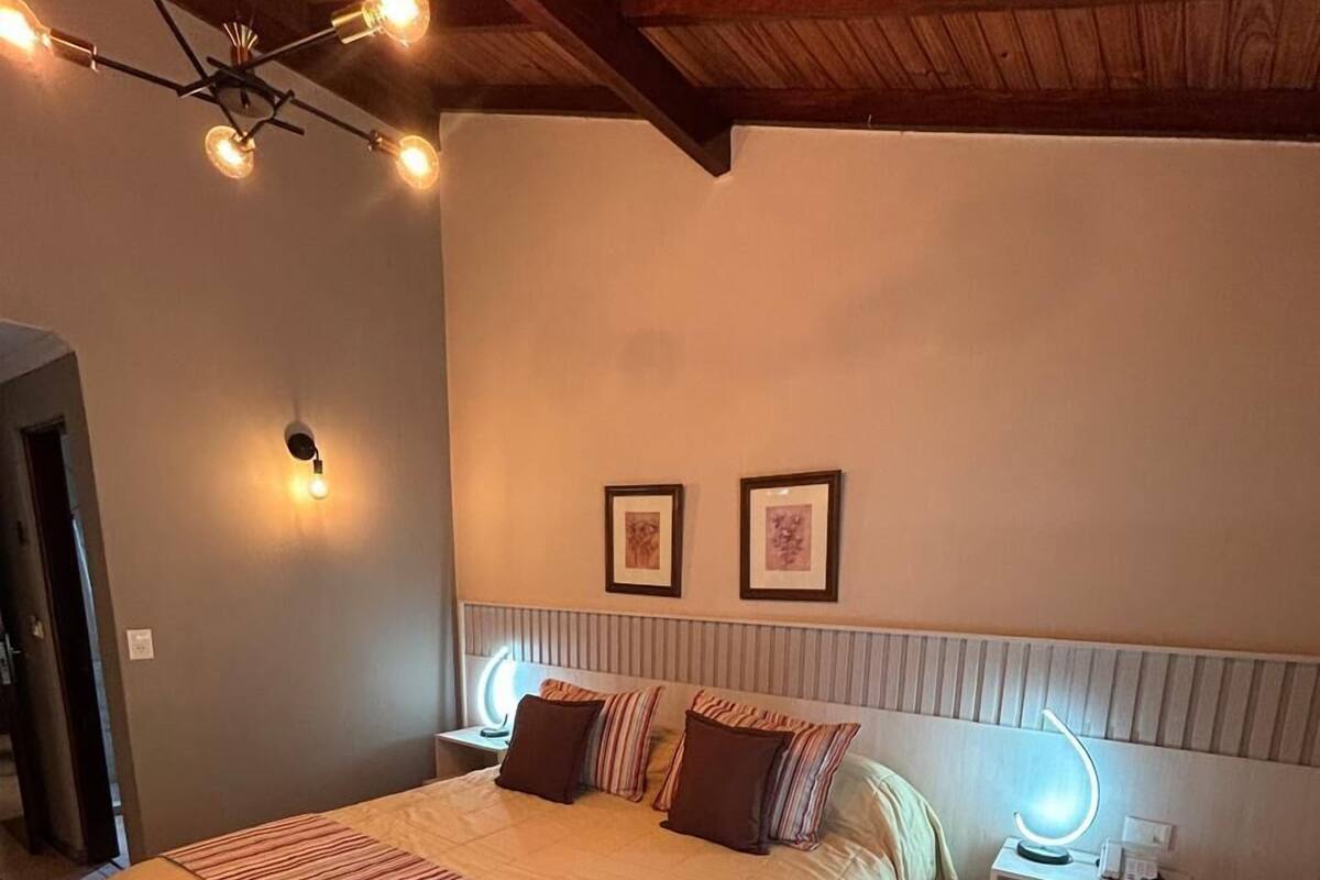 Ein Schlafzimmer mit einem großen Bett, einem Nachttisch mit Lampe, Holzbalken an der Decke und zwei gerahmten Bildern an der Wand.