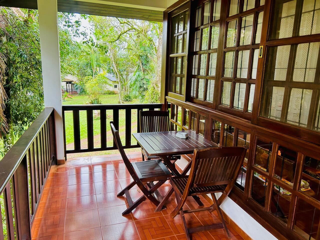 A covered outdoor area with a wooden table and chairs, surrounded by glass windows and a wooden railing.