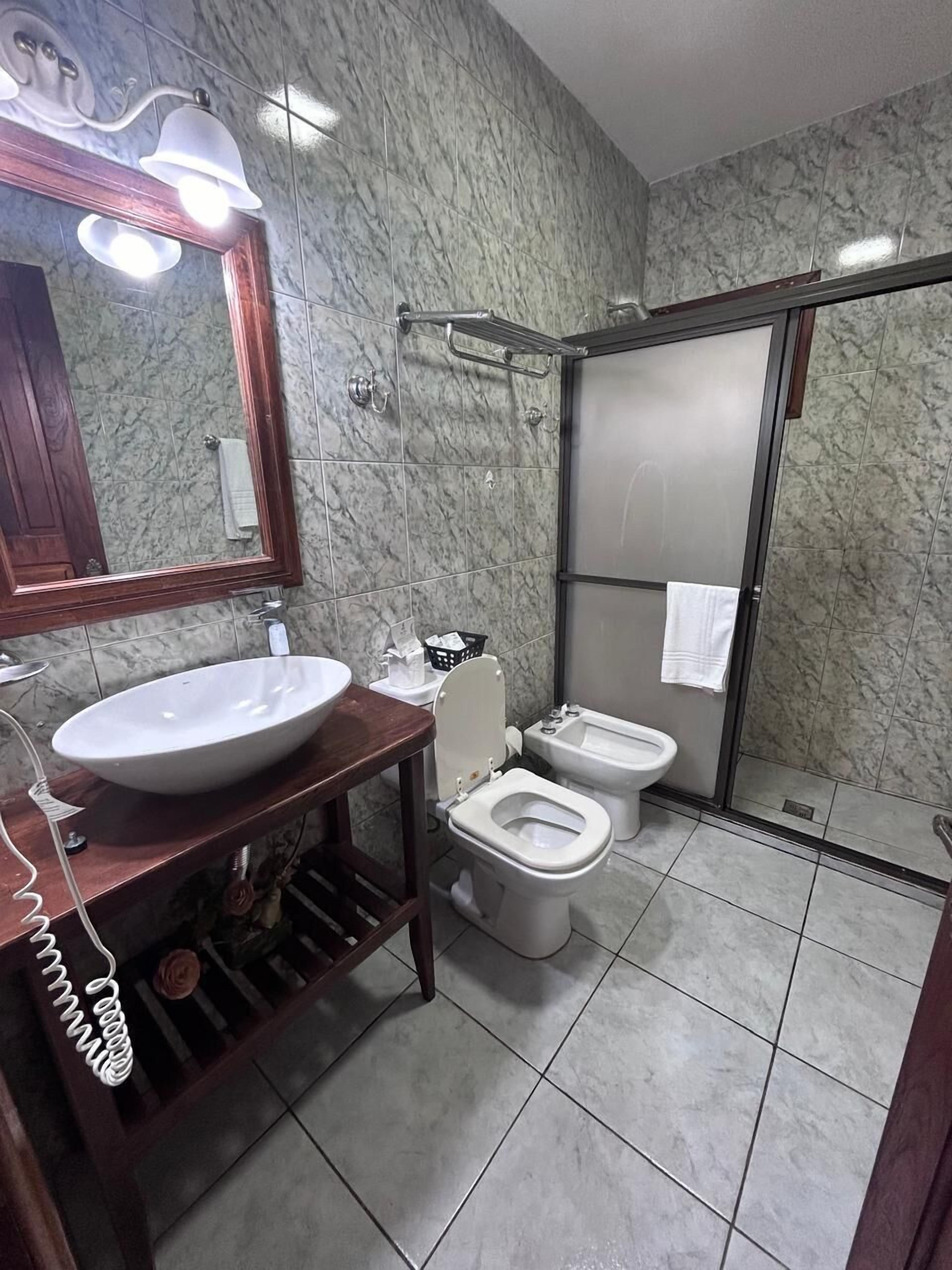 Une salle de bain avec un mur en marbre, un meuble-lavabo en bois avec un évier, deux toilettes et un espace douche.