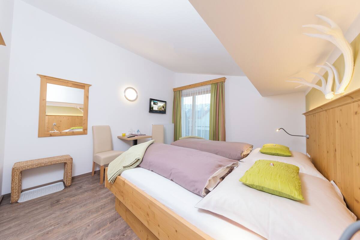 Ein Schlafzimmer mit einem hölzernen Bett, einem kleinen Schreibtisch, einem Stuhl, einer Bank und einem Fenster mit Vorhängen.