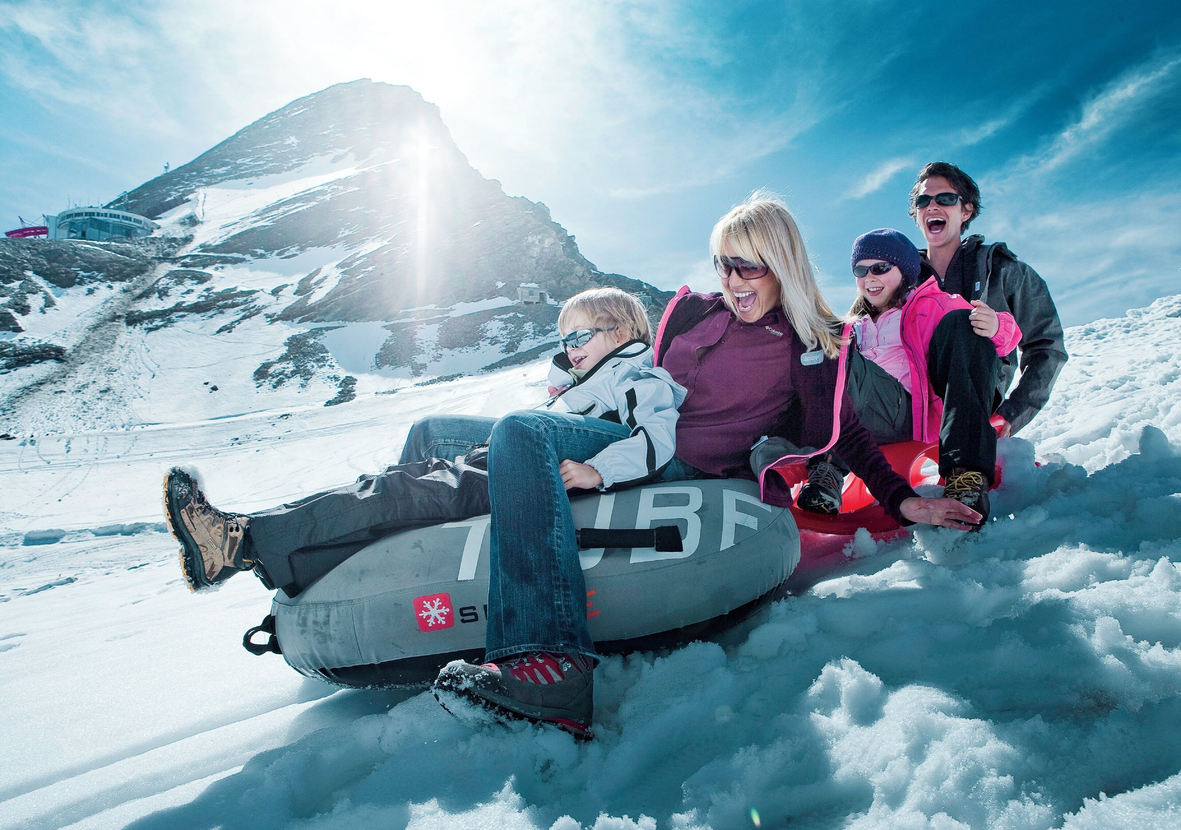 A group of people on a snow tube in a snowy mountainous area.