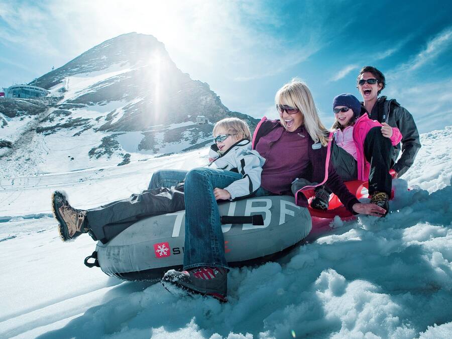 A group of people on a snow tube in a snowy mountainous area.