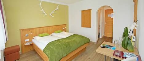 Una habitación con cama, escritorio, silla, mesita, luz empotrada en la pared y una puerta.