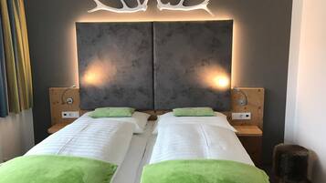 Quarto duplo com duas camas, cada uma com toalhas verdes, uma grande cabeceira fixada na parede com chifres e luminárias de cabeceira.