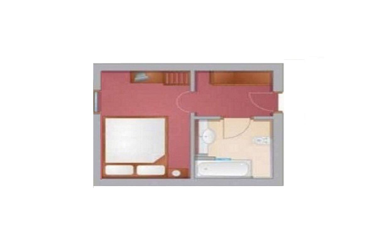 Ein Grundriss eines Hotelzimmers mit einem Bett, einem Badezimmer mit Dusche und einer kleinen Sitzecke.
