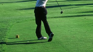 A person playing golf on a course with mountains in the background.