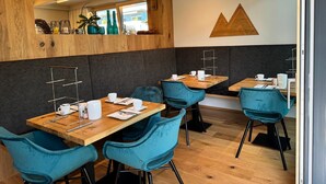 A modern cafe with wooden tables and teal chairs, a wooden accent wall, and a geometric wall decoration.