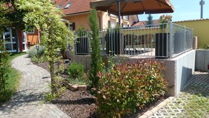 Zona residencial con un sendero pavimentado, un jardín con diversas plantas y un edificio con tejado de tejas y un porche cubierto.