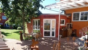 Zona de recepción con fachada roja, puerta de entrada de vidrio y un patio con mobiliario exterior.
