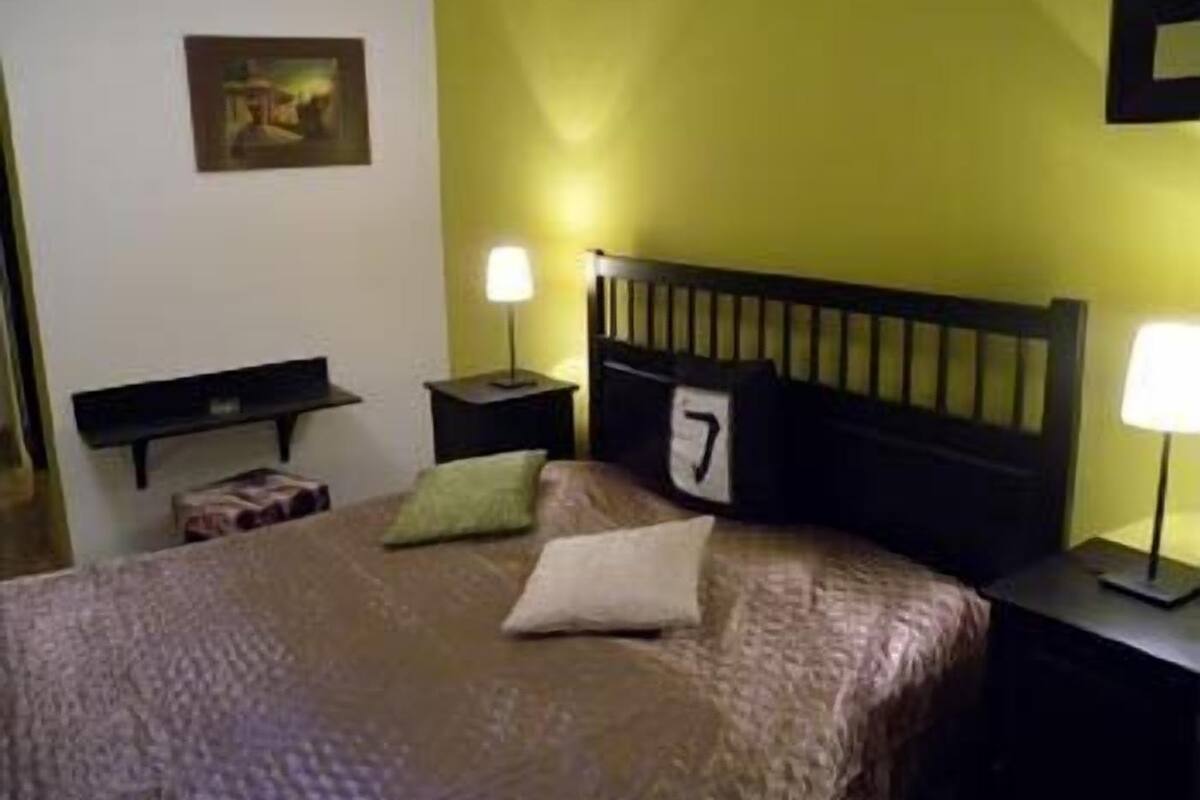 A hotel room with a bed, two bedside tables, a nightstand, a lamp, and a painting on the wall.