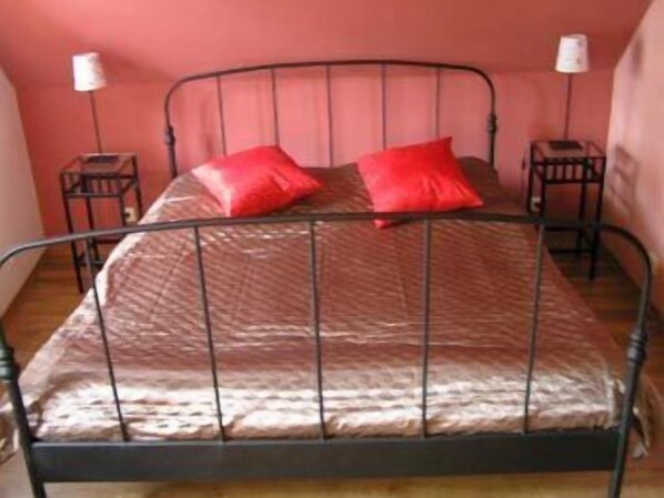 A single bed with a metal frame, two red pillows, and two bedside tables with lamps.