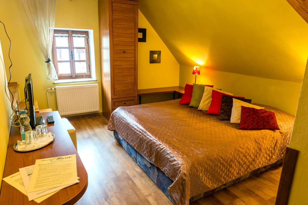 A bedroom with a bed, a desk with papers, a window, and a lamp.