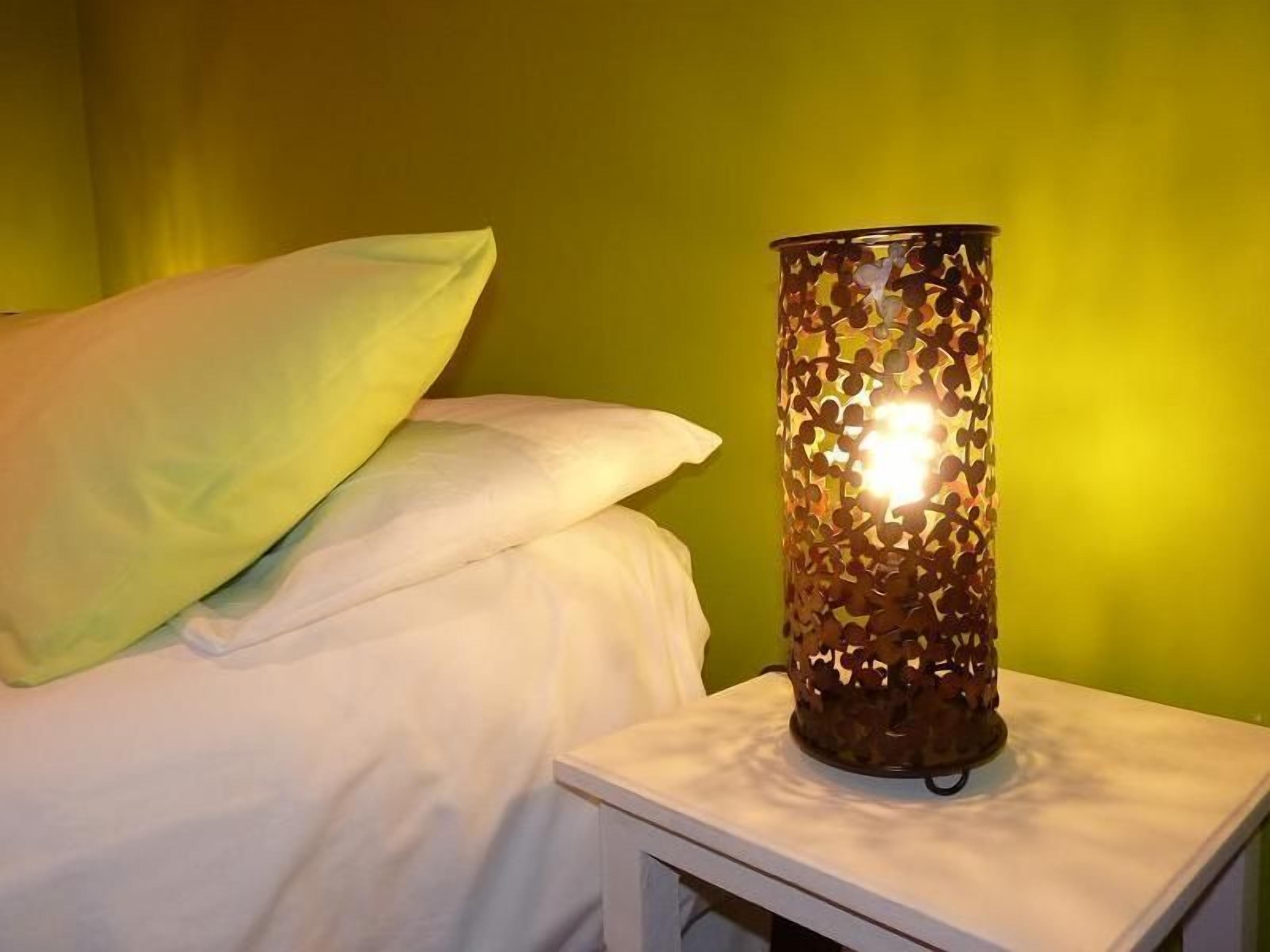 A bed with white bedding and a decorative lamp with a patterned shade on a bedside table.