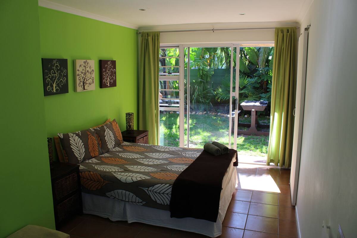 Un dormitorio con cama, paredes verdes y puerta corrediza de vidrio a un jardín.