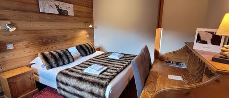 Ein Zimmer mit Holzboden, einem Bett, einem Schreibtisch und einer Lampe.