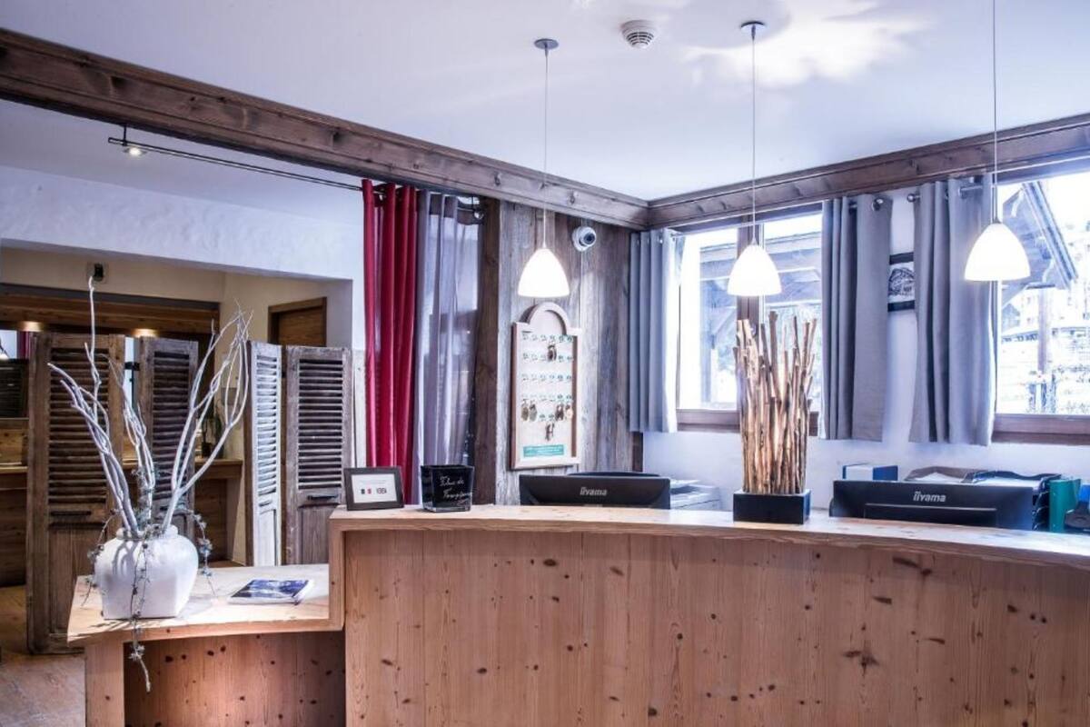 A wooden reception desk with pendant lighting, a vase with branches, and a framed picture on the wall.