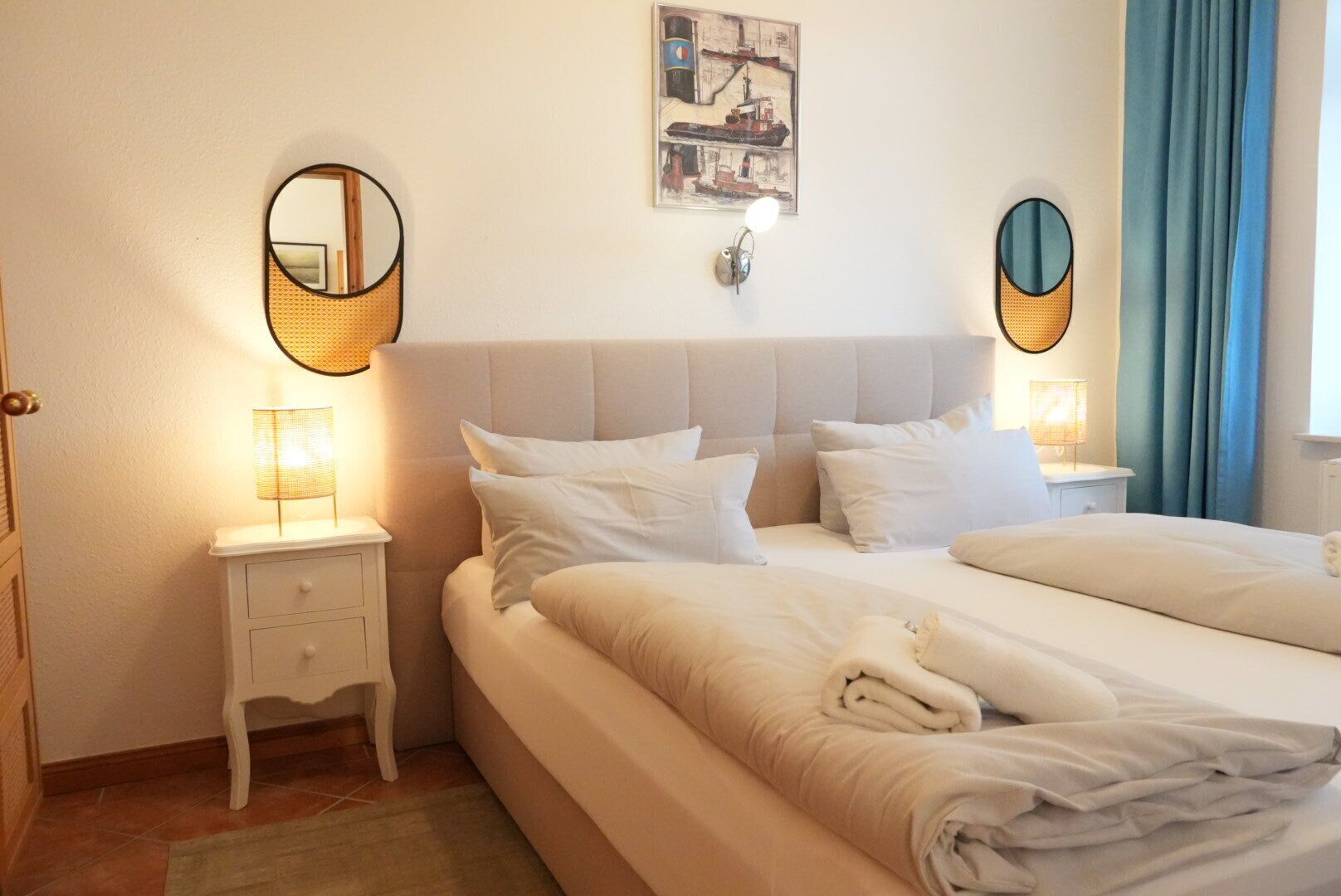 Une chambre d’hôtel avec un grand lit, deux tables de chevet, une lampe fixée au mur et un tableau.