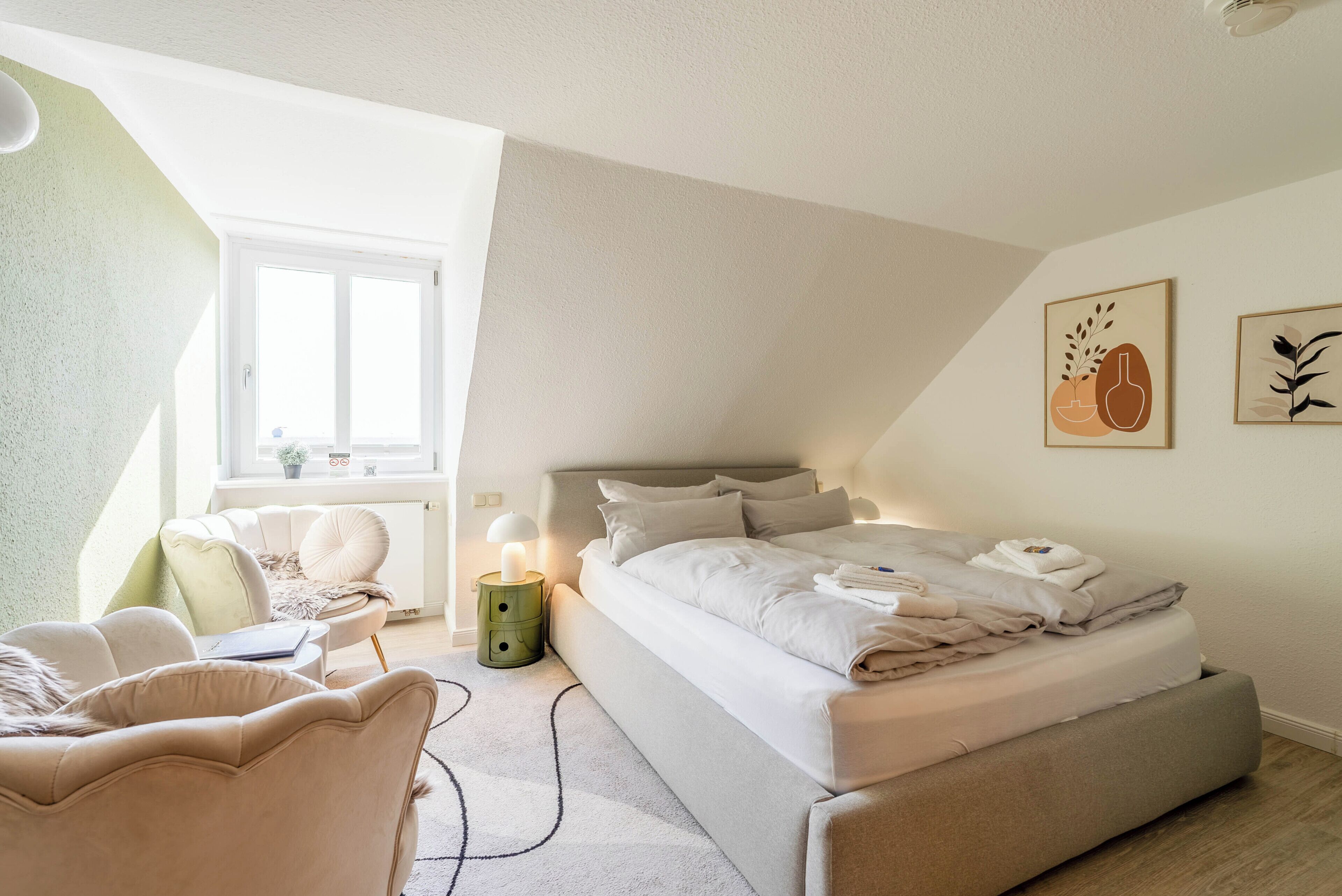 Um quarto com uma cama, uma cadeira, uma mesa de cabeceira, uma luminária e obras de arte na parede.