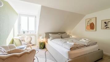 Um quarto com uma cama, uma cadeira, uma mesa de cabeceira, uma luminária e obras de arte na parede.