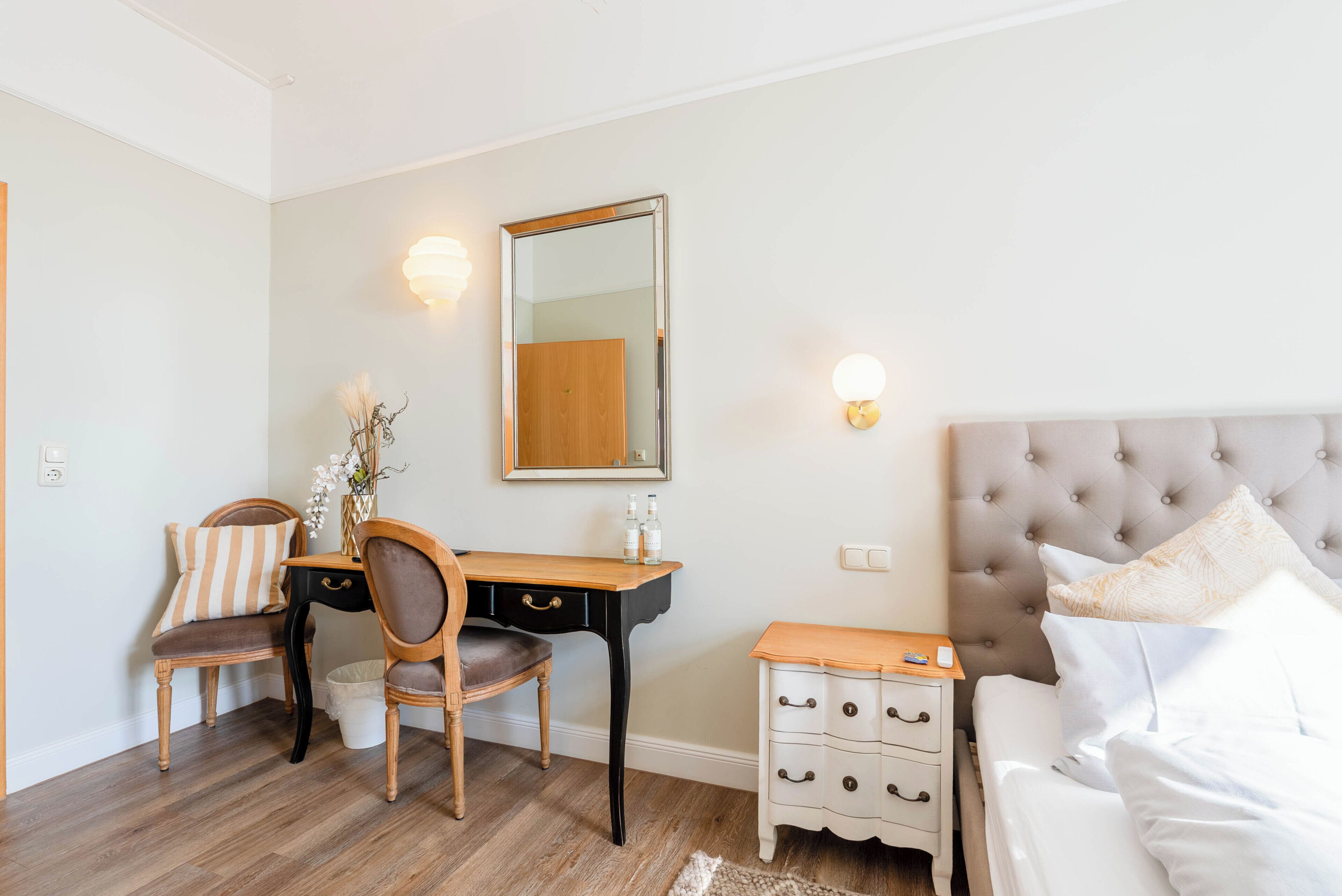 A bedroom with a bed, bedside table, nightstand, dresser, desk, chair, and a mirror.