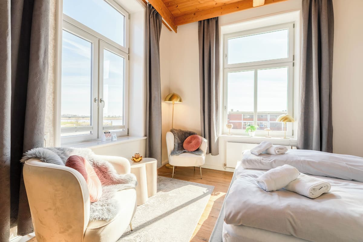 A hotel room with a bed, a chair, a lamp, and a view of the city.
